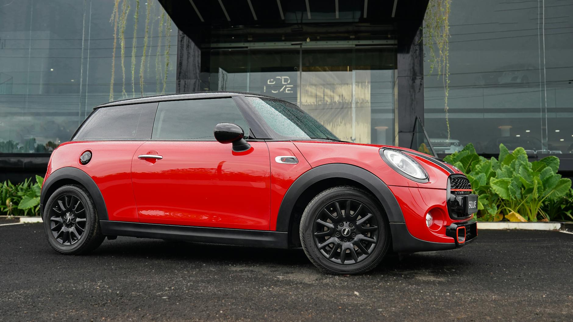 Czerwony Mini Cooper zaparkowany przed nowoczesnym budynkiem w deszczu