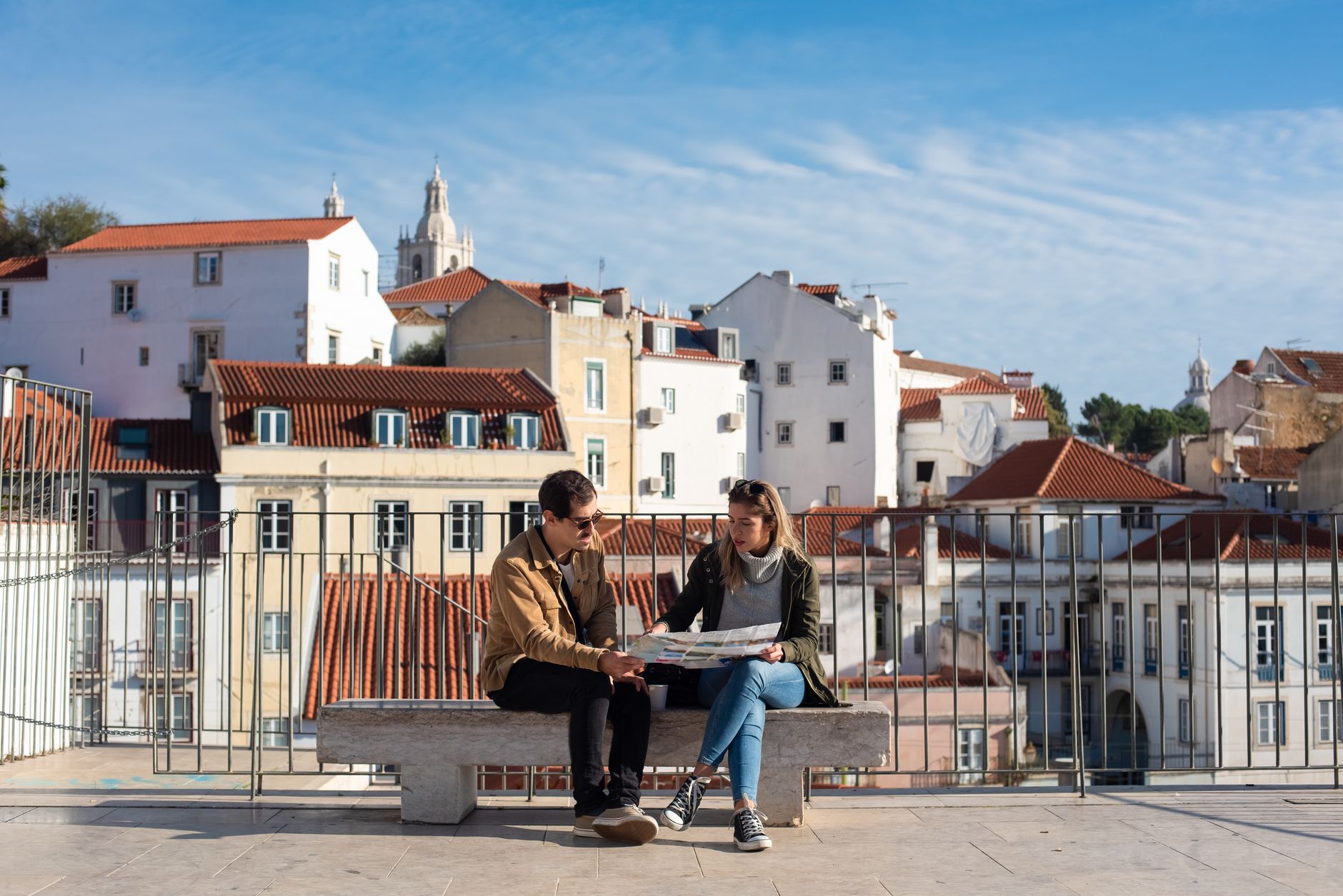 Lizbona na weekend – co zobaczyć i jak zaplanować idealną city break w Portugalii Para na ławce ogląda mapę z panoramą dachów Lizbony w tle