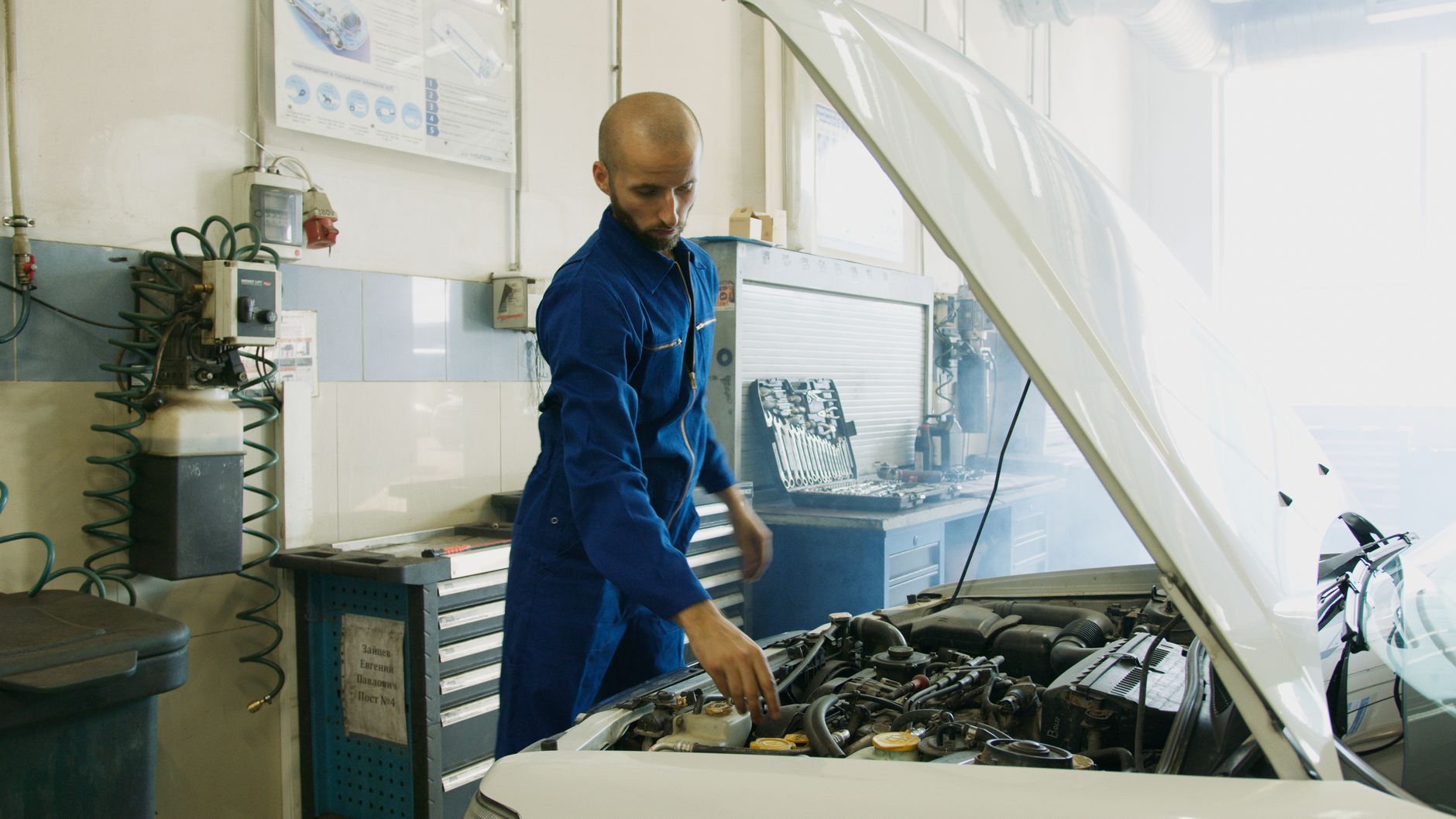 Mechanik w niebieskim kombinezonie sprawdza silnik Subaru Impreza w warsztacie