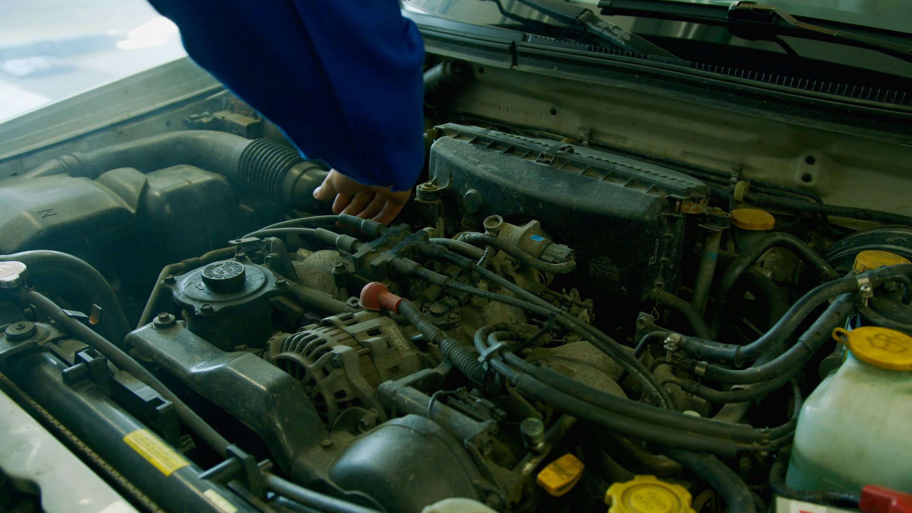 Mechanik w niebieskim kombinezonie sprawdza silnik Subaru w garażu