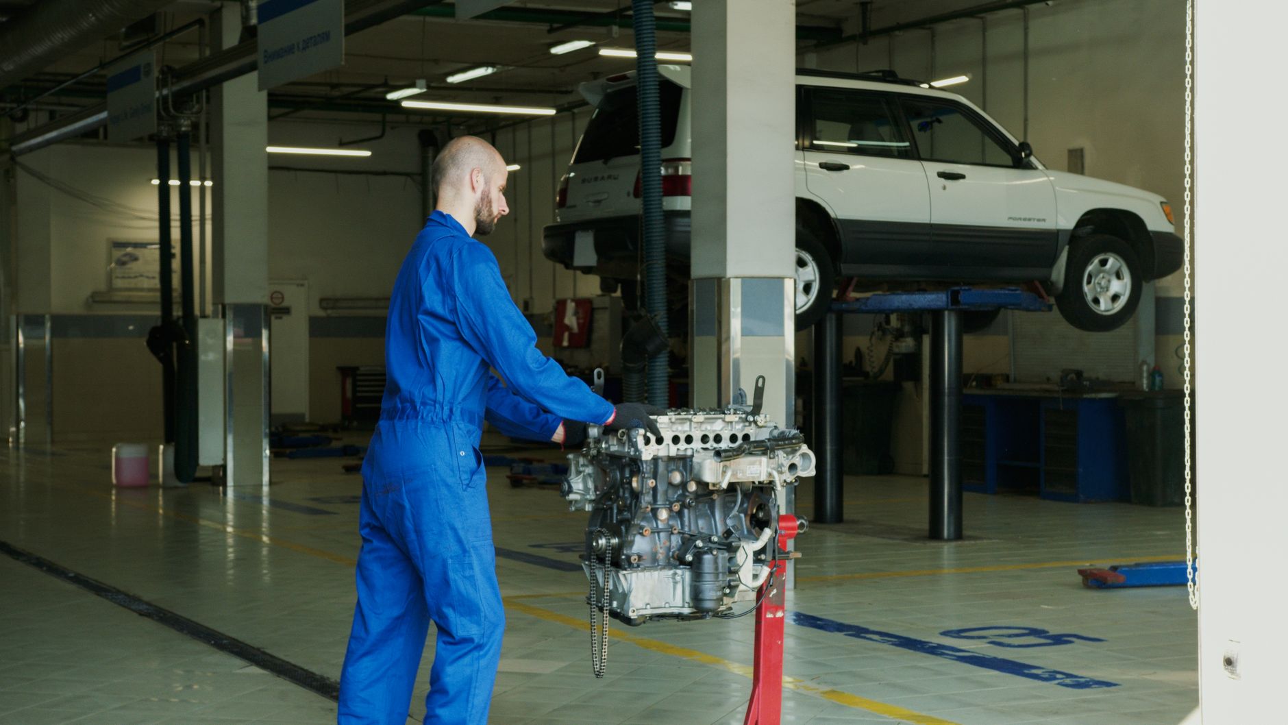 Mechanik w niebieskim kombinezonie sprawdza silnik Subaru w garażu