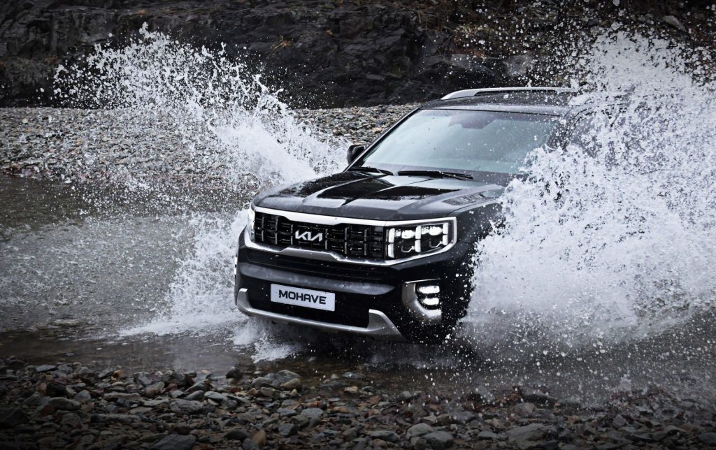 SUV Jeep brodzi w skalistym potoku, rozpryskując wodę w terenie